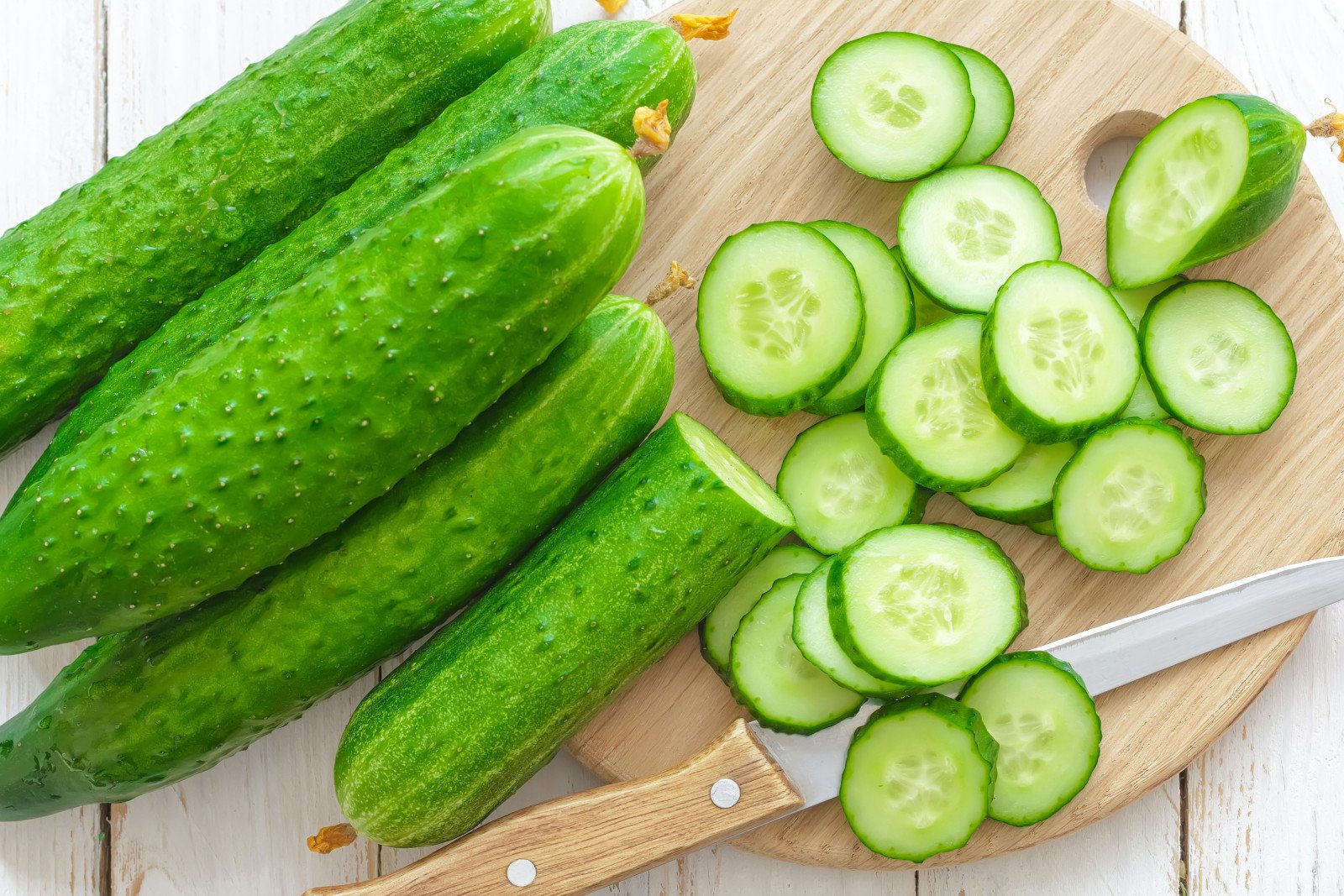 Several cucumbers on a cutting board with cucumber slices and a knife.