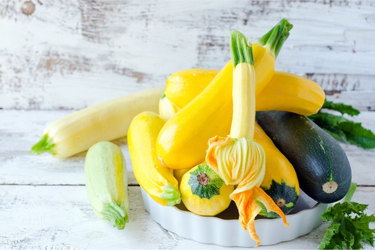 Yellow summer squash and zucchini in a white tart dish with a wooden white background.