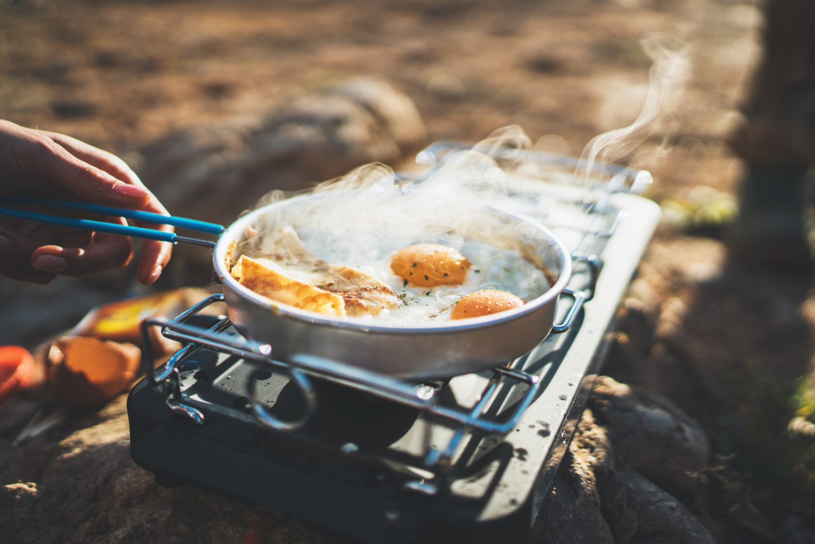 Man's hand cooking eggs in a frying pan over a camping stove.