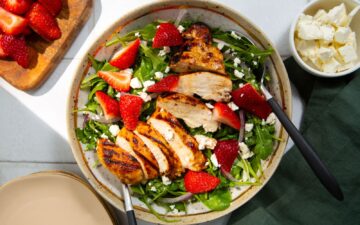 Fresh green salad topped with feta cheese, strawberries, and grilled chicken on a tan and white plate with a white background and a green napkin.