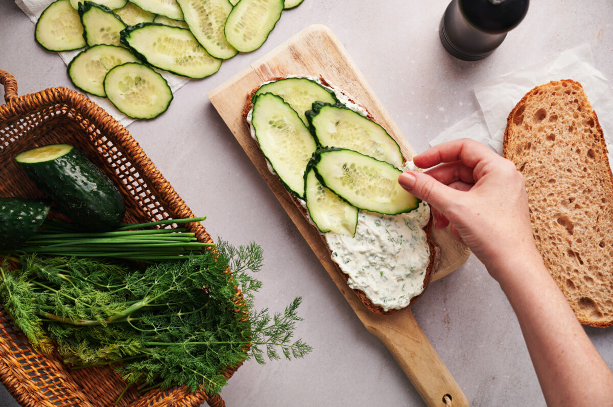 Woman's hand adding cucumber slices to a slice of bread.