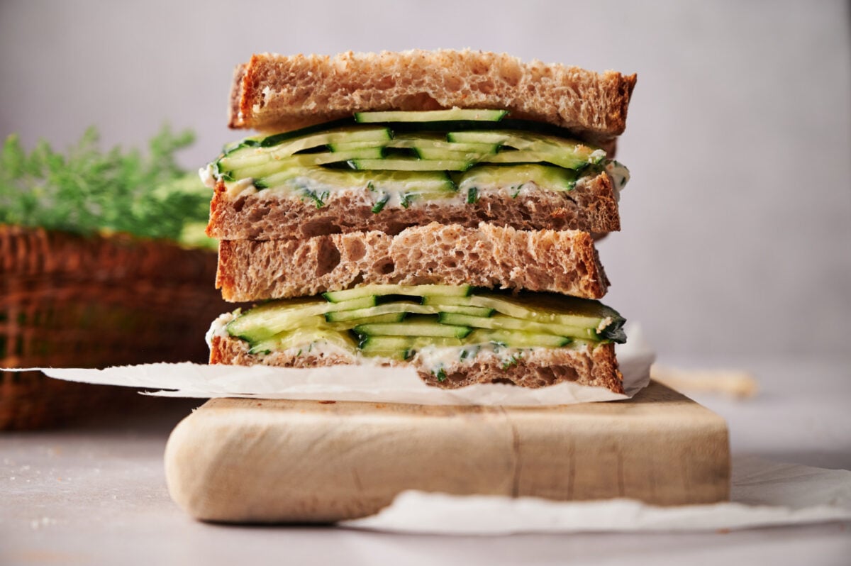 A cucumber sandwich cut in half and stacked on a cutting board.
