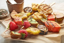 Grilled fruit kabobs on skewers on parchment paper.