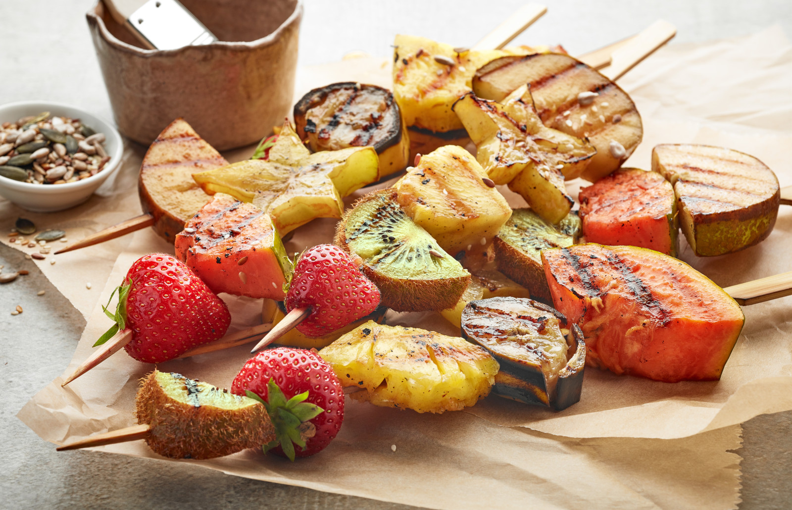 Grilled fruit kabobs on skewers on parchment paper.