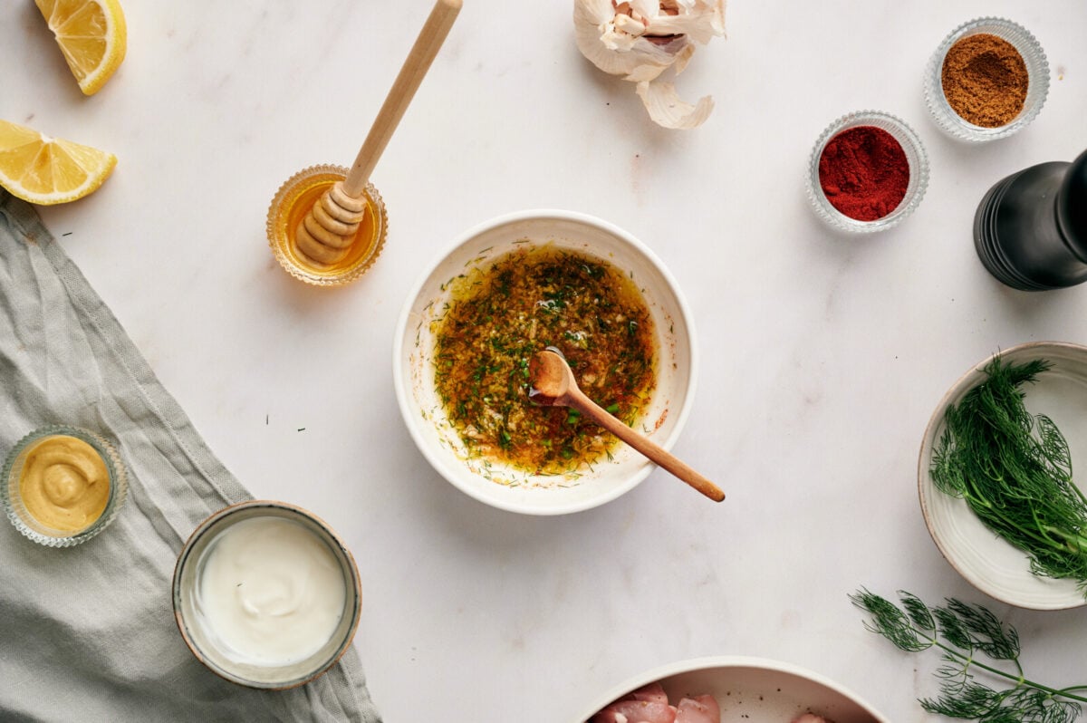 A lemon and dill chicken marinade in a white bowl with a wooden spoon.