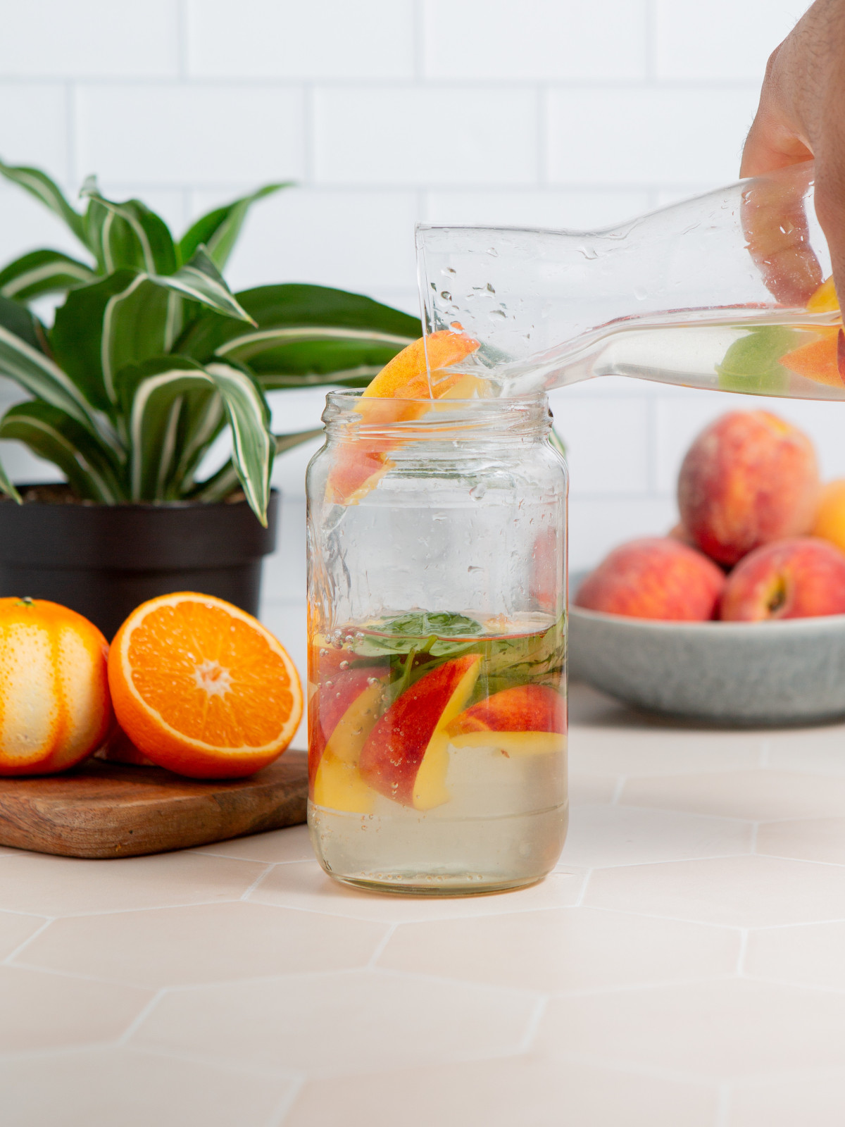Peach infused water with basil being poured from a glass pitcher into a glass jar.