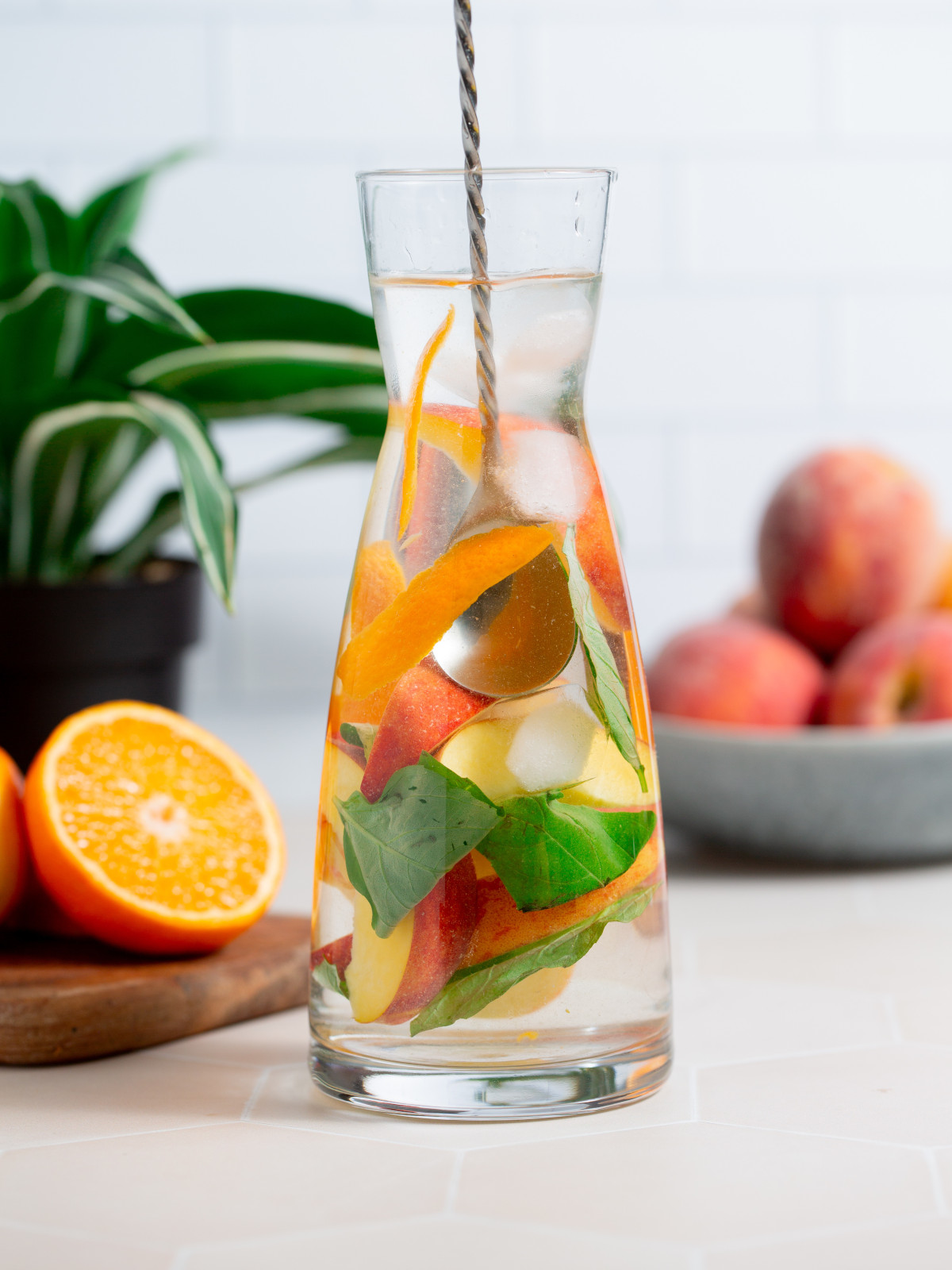 Peach infused water with basil in a glass pitcher being mixed with a spoon.