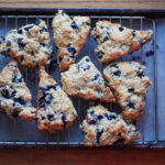 Blueberry scones on a cooking rack that's on top of a parchment-lined baking sheet.