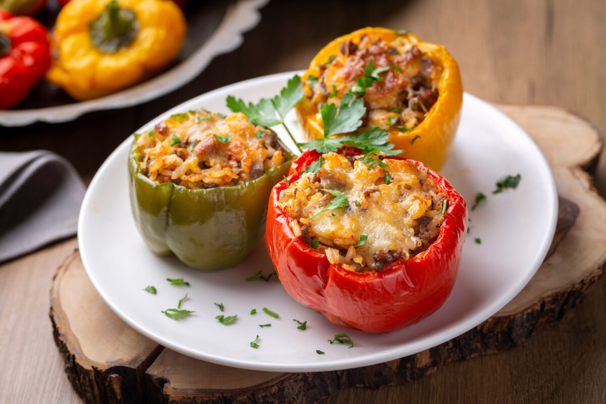 Green, yellow, and red stuffed bell peppers on a white plate garnished with parsley.