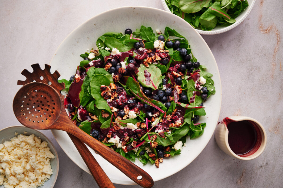 Top flat-lay view of summer blueberry salad with blueberries, feta, and toasted pecans in a white bowl with wooden utensils.