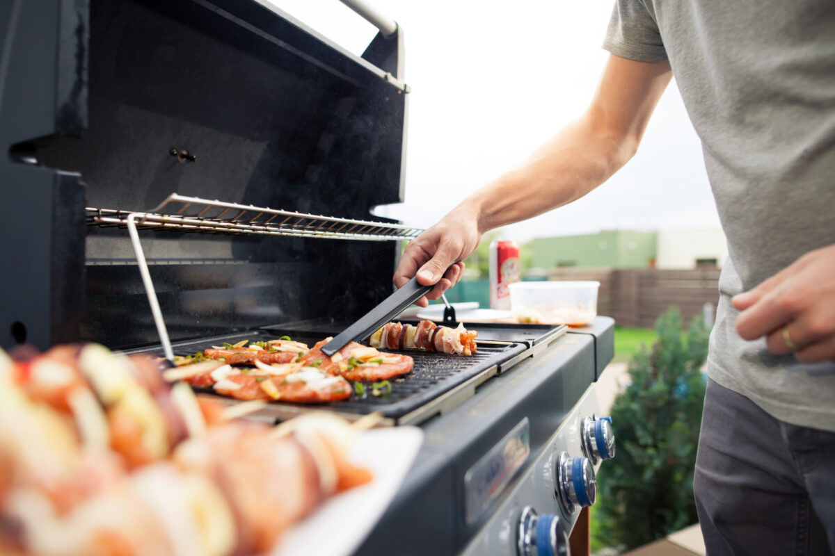 A young man's arm arranging food on a BBQ grill.