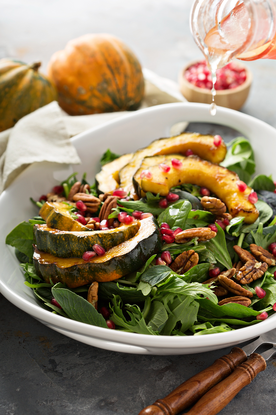 A white bowl filled with roasted acorn squash, spinach, and pomegranates with Acorn squash in the background.