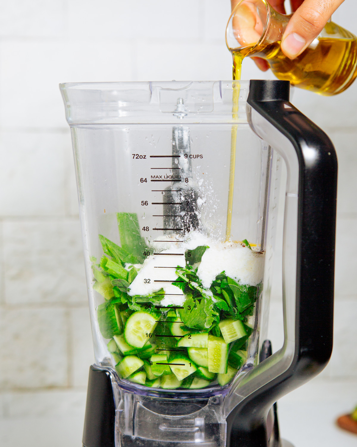 Ingredients for cold cucumber soup being added to a blender pitcher.