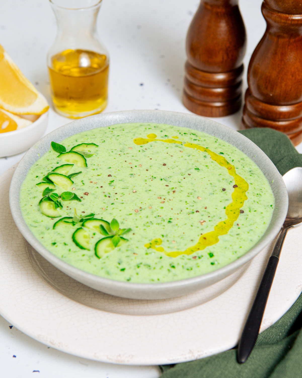 Cold cucumber soup in a white bowl garnished with sliced cucumbers and olive oil.