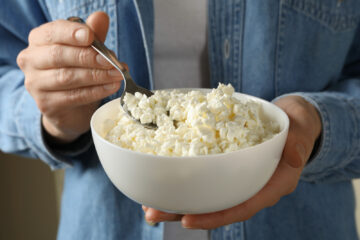 Woman's hands holding a white bowl filled with cottage cheese and scooping out some with a spoon.