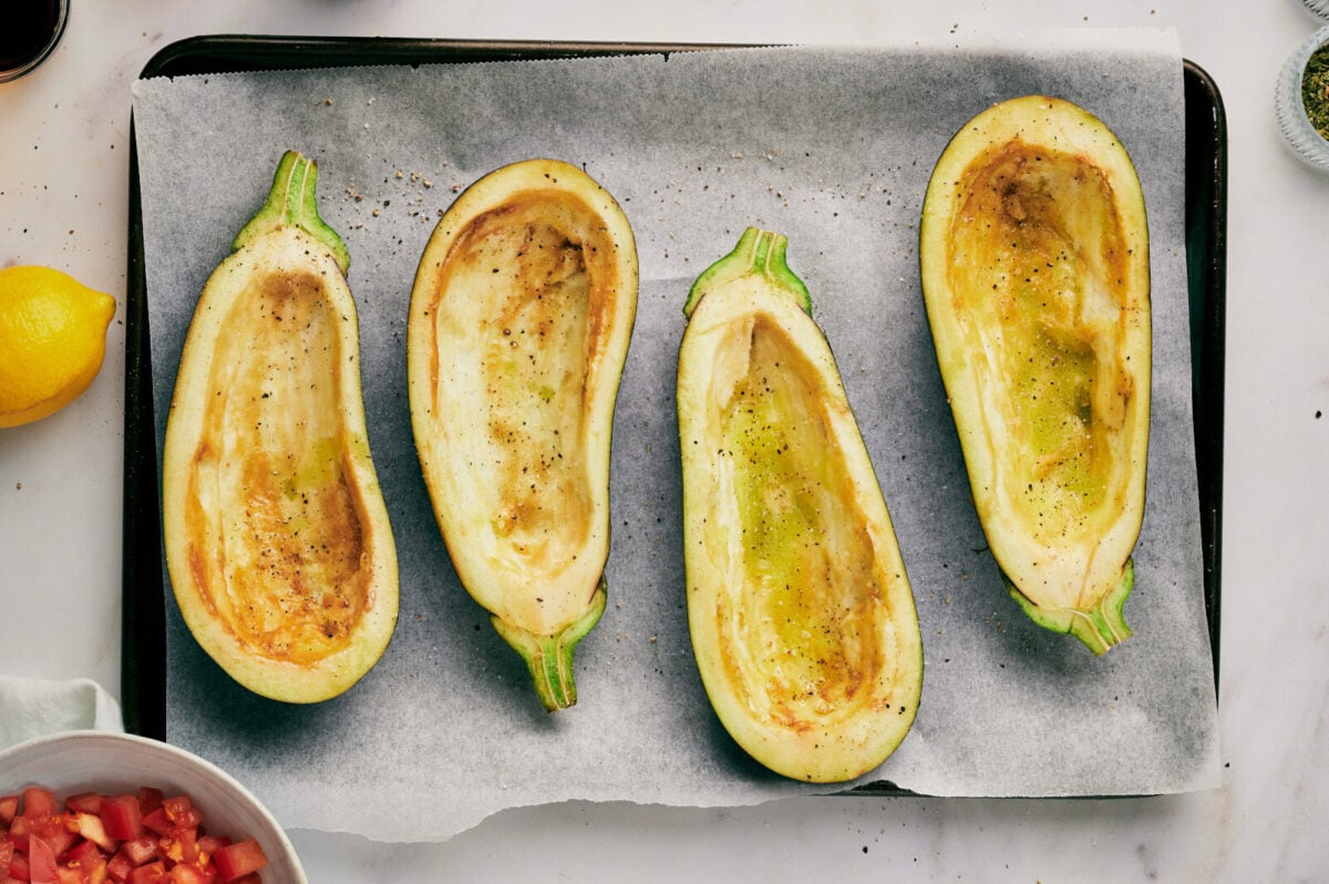 Four eggplants with seeds scooped out on a parchment lined baking sheet.
