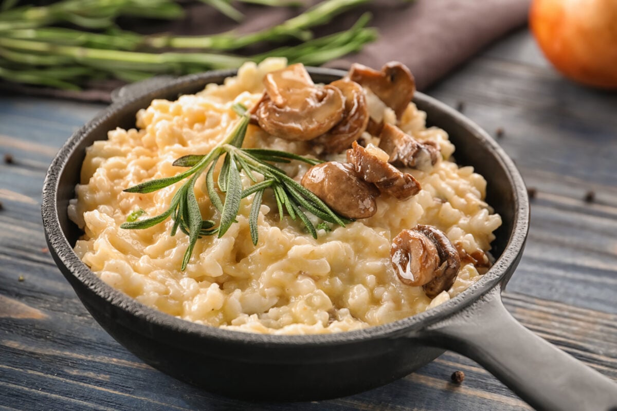 Creamy risotto in a black skillet garnished with rosemary and sautéed mushrooms.