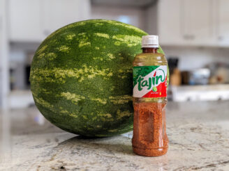 A bottle of Tajin chili lime seasoning with a watermelon behind it.
