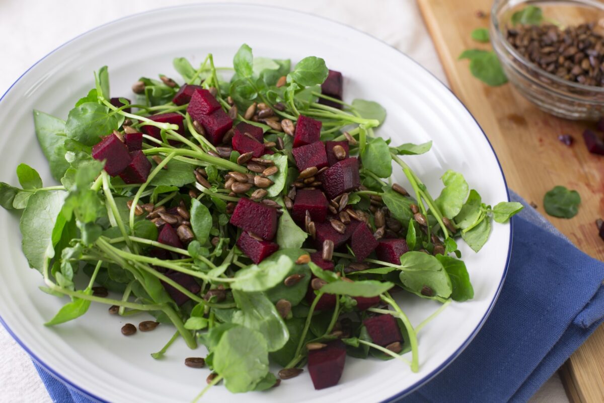 A watercress salad with beets and sunflower seeds in a white bowl with a blue napkin.