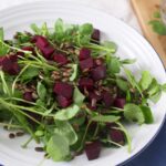 A watercress salad with beets and sunflower seeds in a white bowl with a blue napkin.