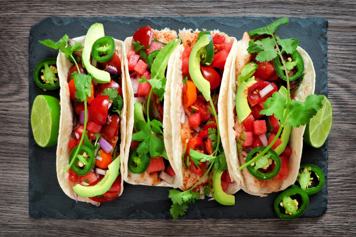 Spicy fish tacos with watermelon salsa and avocados, overhead view on slate server.