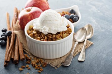 A white bowl with a serving of apple crispy and topped with ice cream.