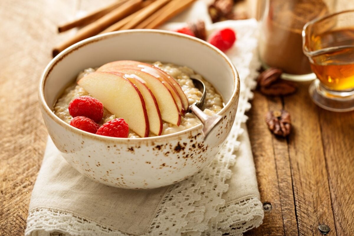 A bowl of oatmeal with sliced apples and raspberries with a wooden background.
