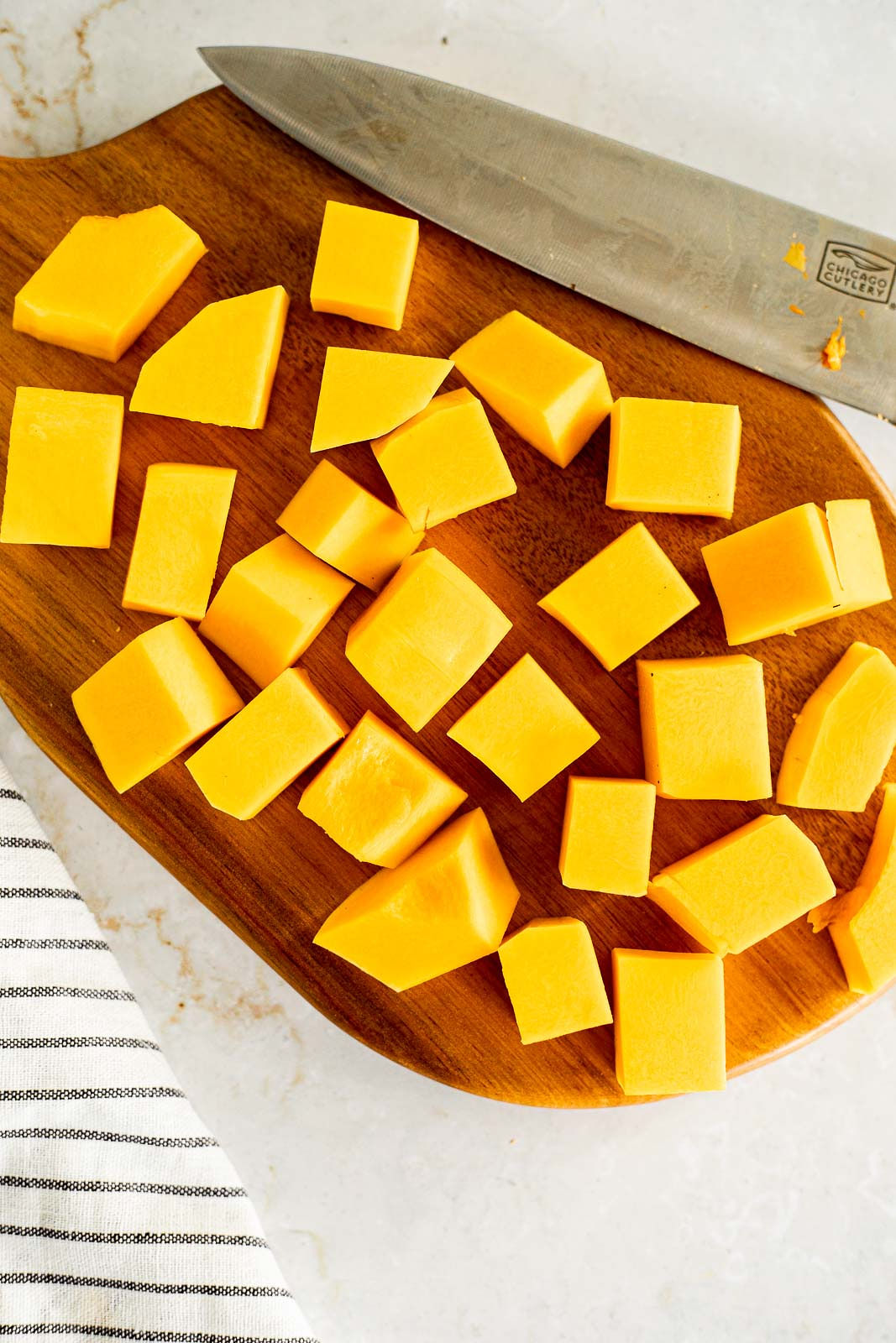 Butternut squash cut into cubes on a cutting board with a chef's knife.
