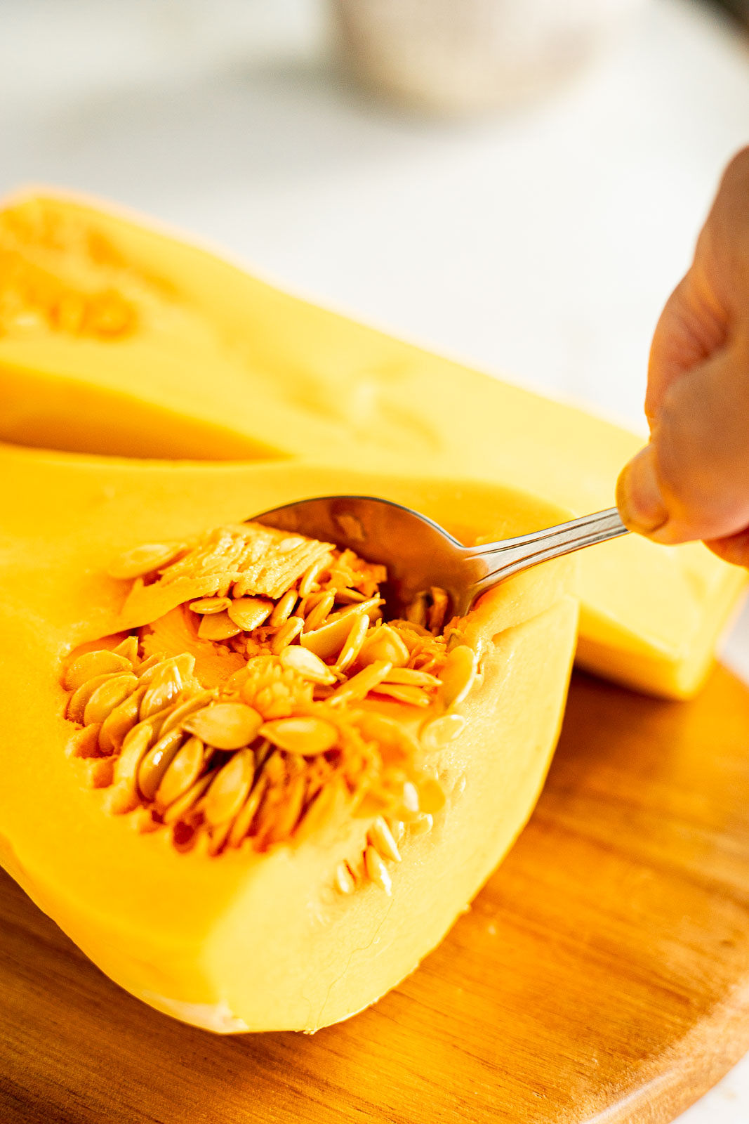 Scooping out the seeds of a butternut squash with a spoon.