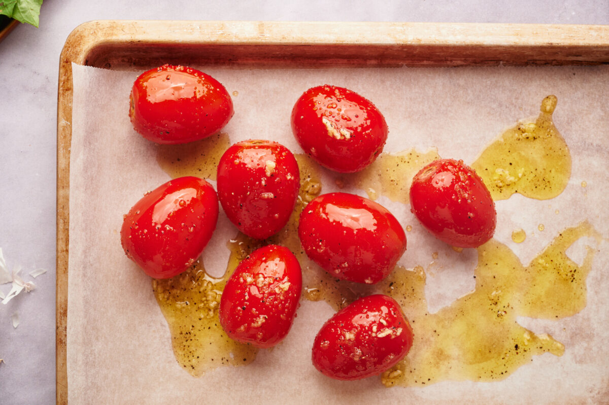 Seasoned plum tomatoes drizzled with olive oil on a parchment lined baking sheet.