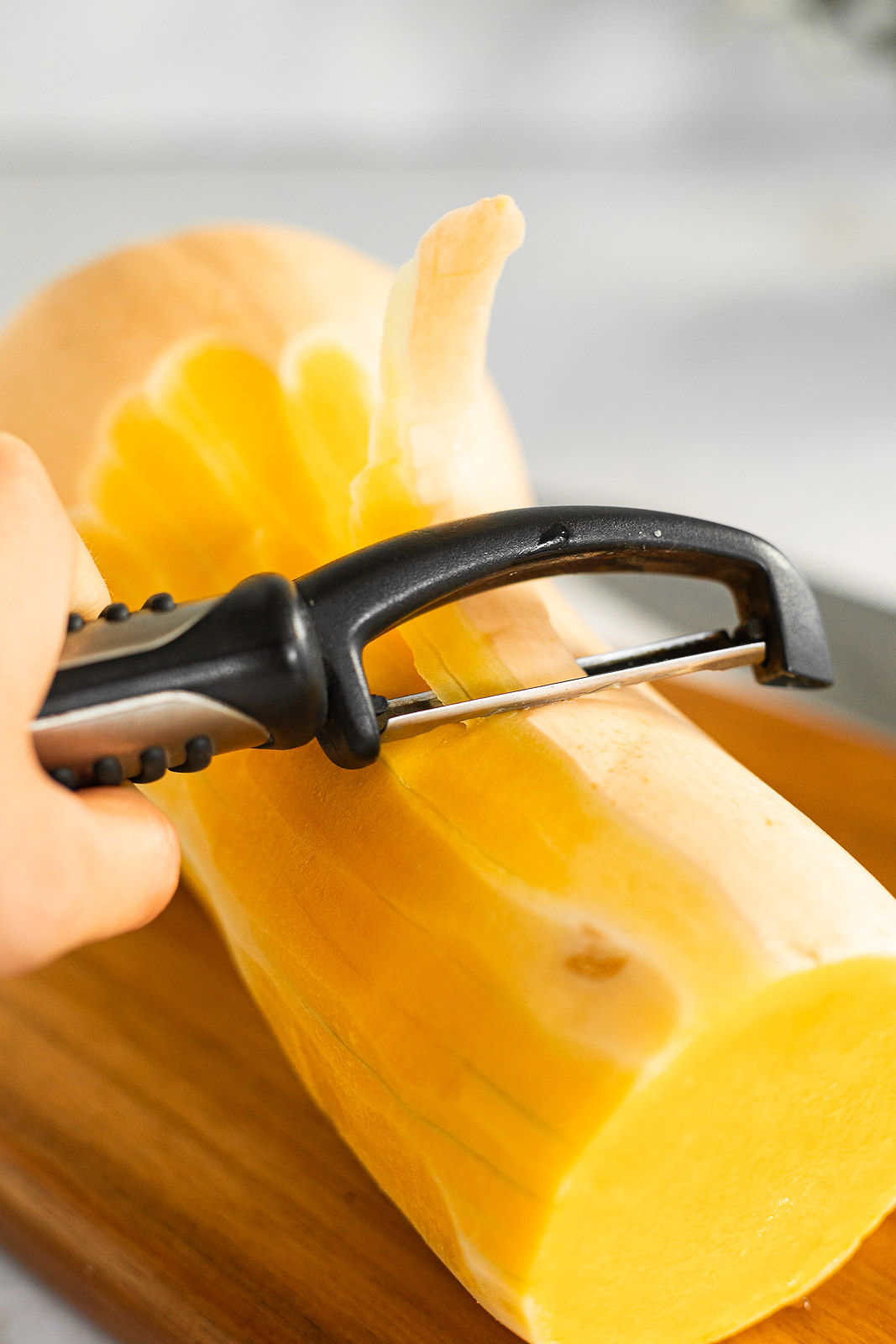 A vegetable peeler peeling the skin off of a butternut squash.