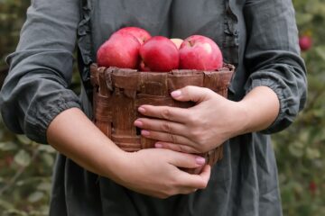 A woman holding a basket of apples outside.
