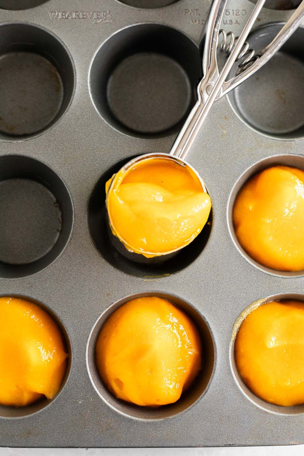 Scooping pureed butternut squash into a muffin tin.