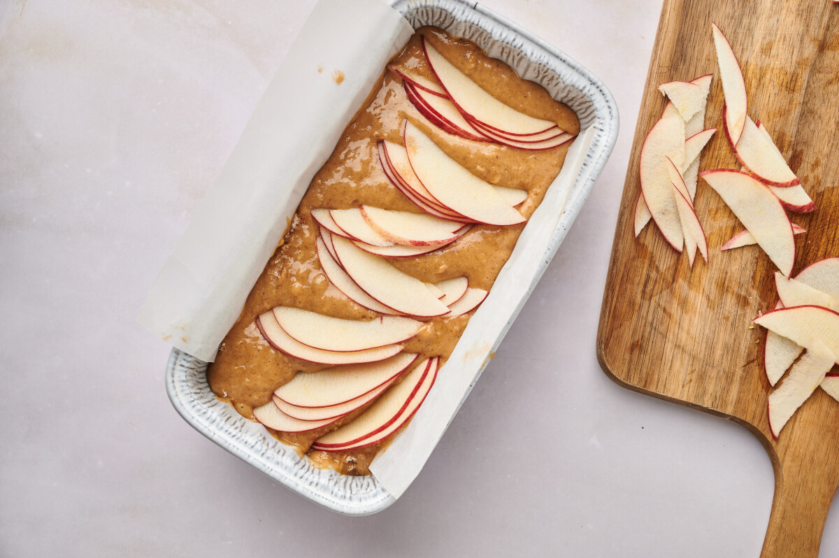 Slices of apple on top of apple bread batter in a parchment lined loaf pan.