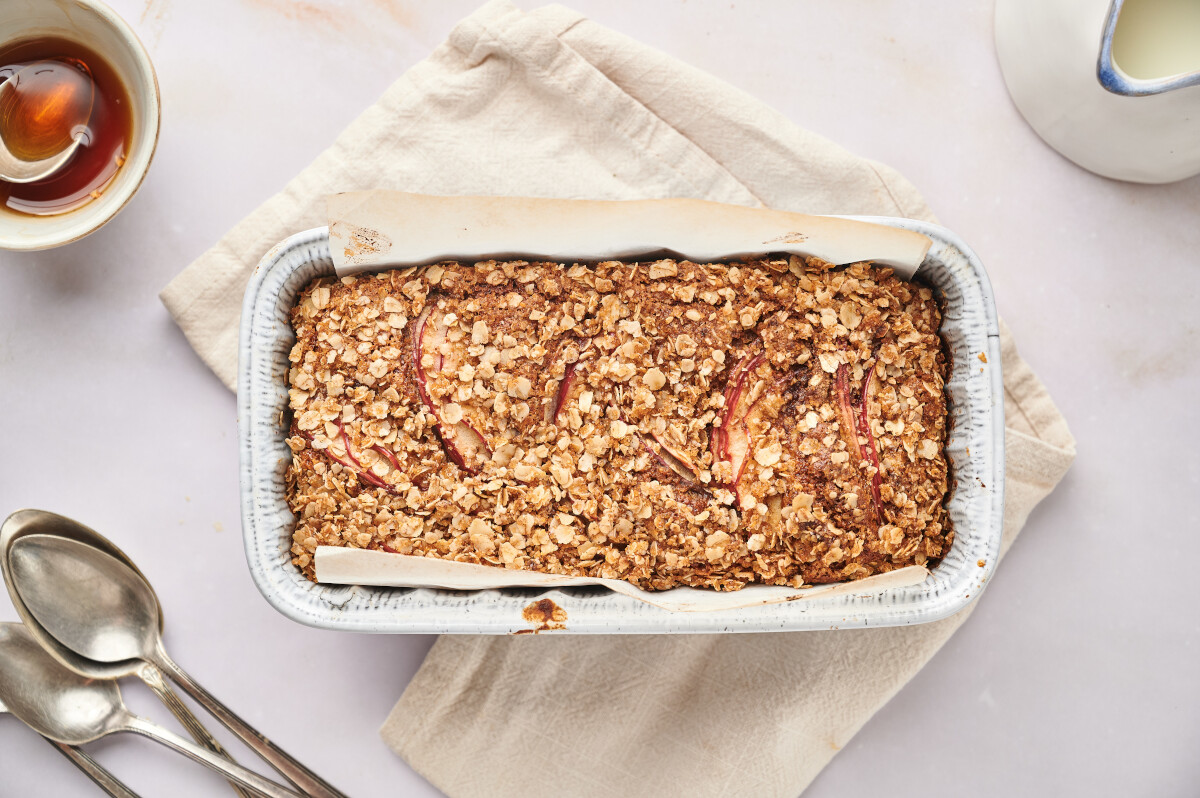 Healthy apple bread baked to perfection in a loaf pan with a napkin and spoons and maple syrup. 