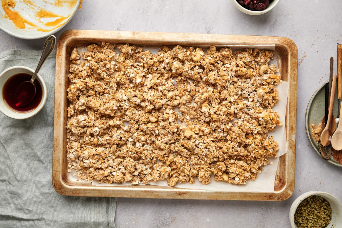 Pumpkin Spice Granola spread out on a parchment lined baking sheet, ready to go in the oven.