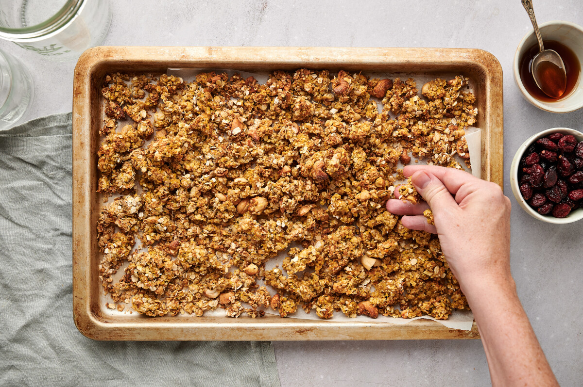 Breaking up larger pieces of Pumpkin Spice Granola over a baking sheet.