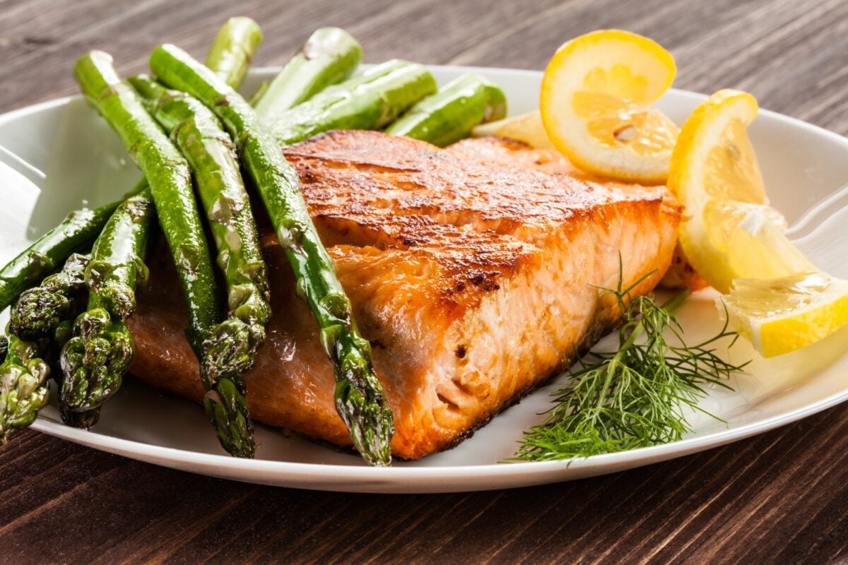 A plate with roasted salmon, asparagus, dill, and lemon slices.