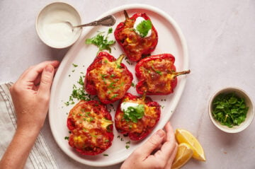 Southwestern stuffed peppers served with sour cream and cilantro on a platter with hands holding it.