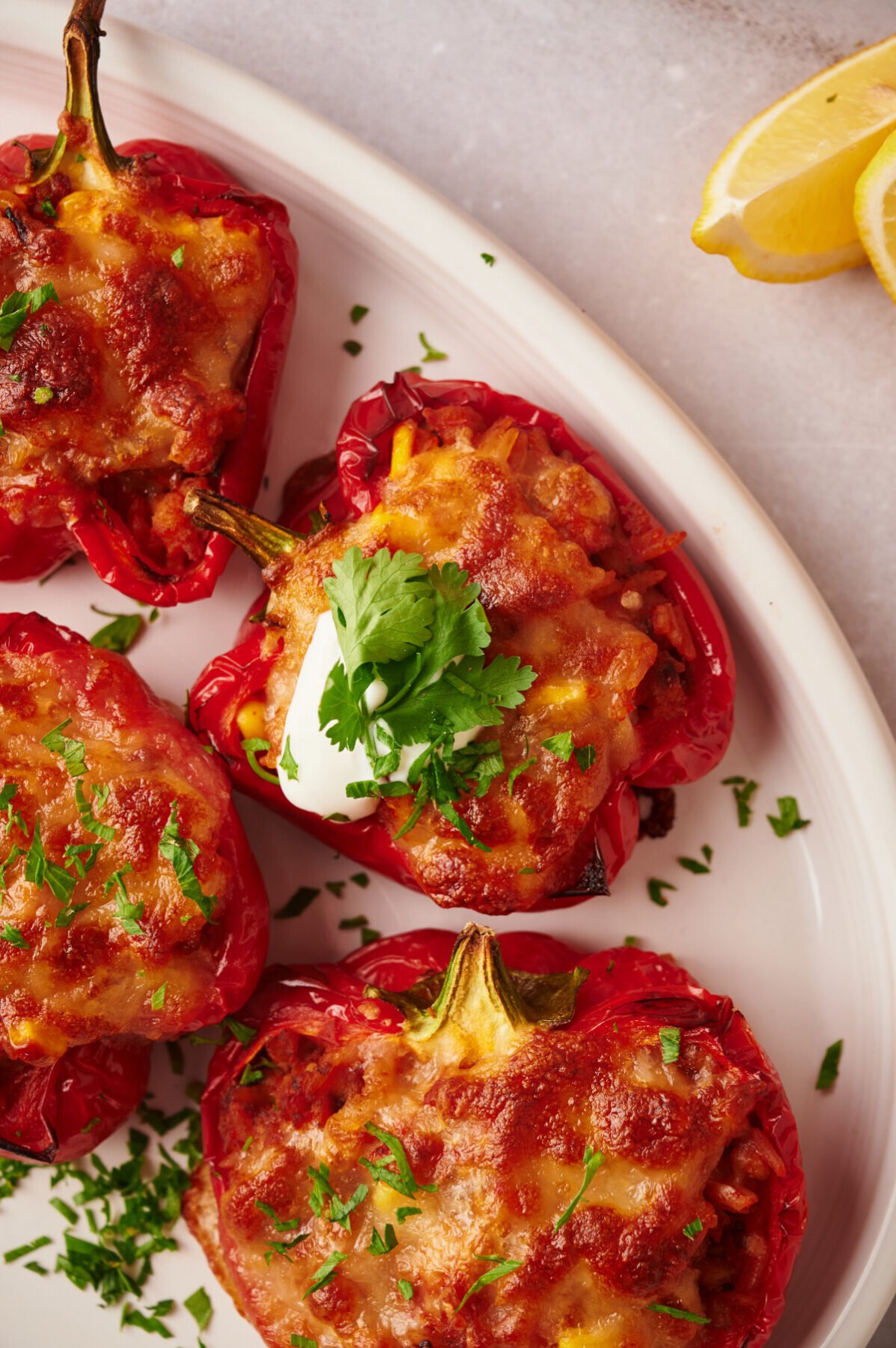 Southwestern stuffed peppers on a white plate served with sour cream and cilantro with lemon wedges on the side.