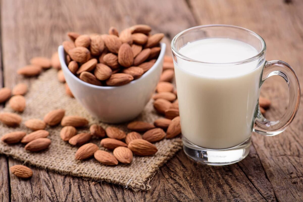 Almonds in a bowl next to a glass of almond milk.