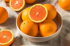 Several Cara cara navel oranges, some whole and some cut in half, and some in a bowl and some on a table with a white tablecloth.