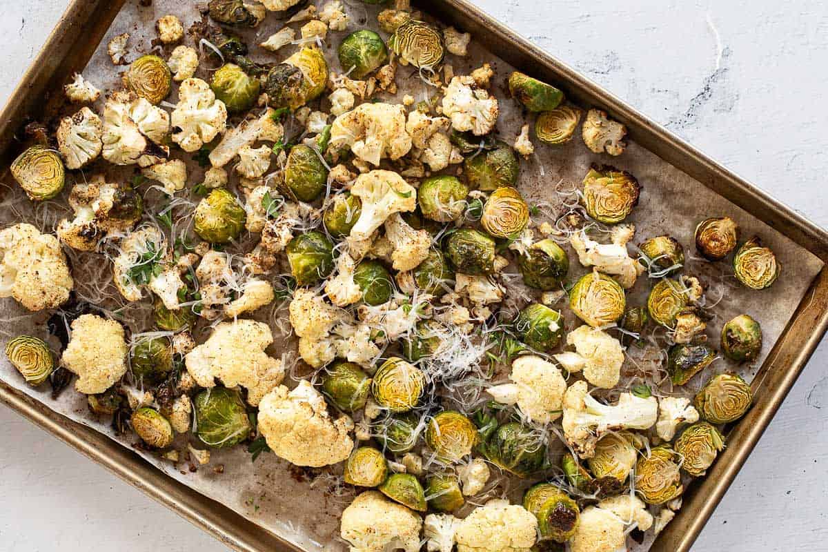 Roasted Cauliflower & Brussels Sprouts on a parchment lined baking sheet with shredded Parmesan cheese.