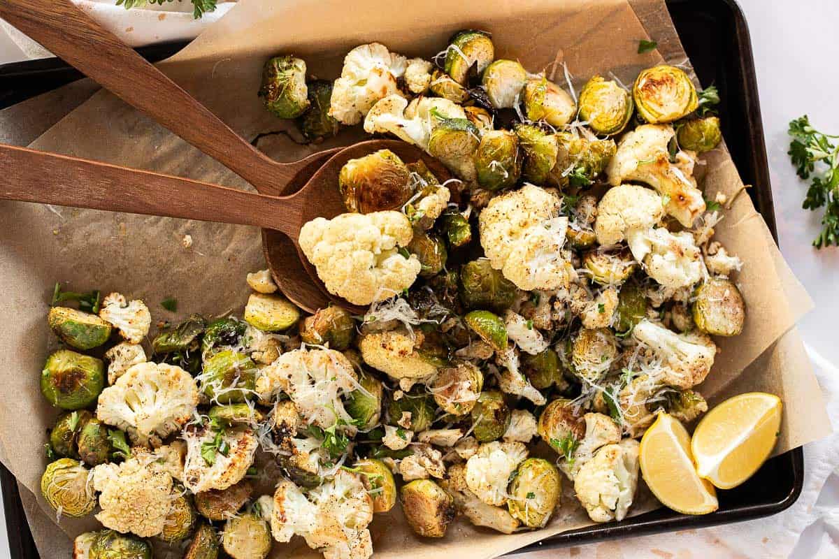 Roasted Cauliflower & Brussels Sprouts on a parchment lined baking sheet being served with wooden spoons.