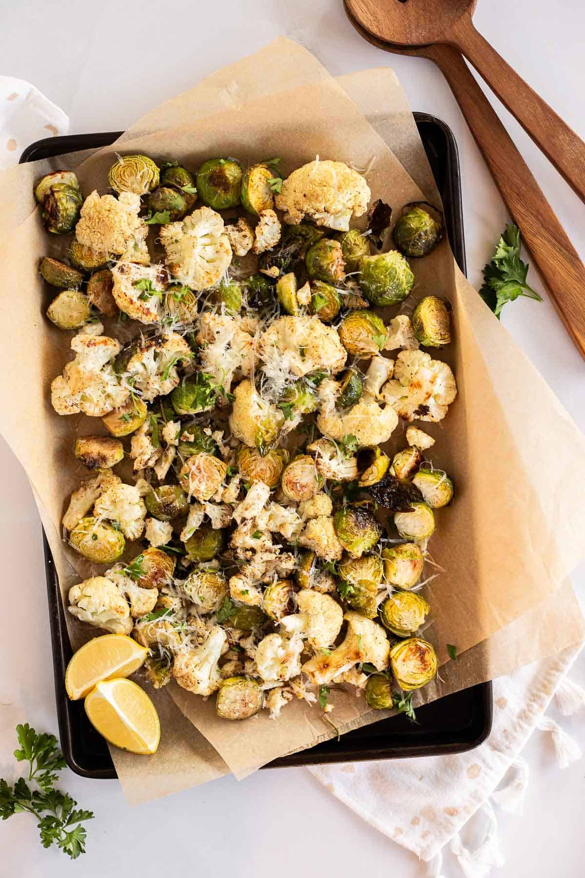 Roasted cauliflower & Brussels sprouts with Parmesan cheese on a parchment lined baking sheet.