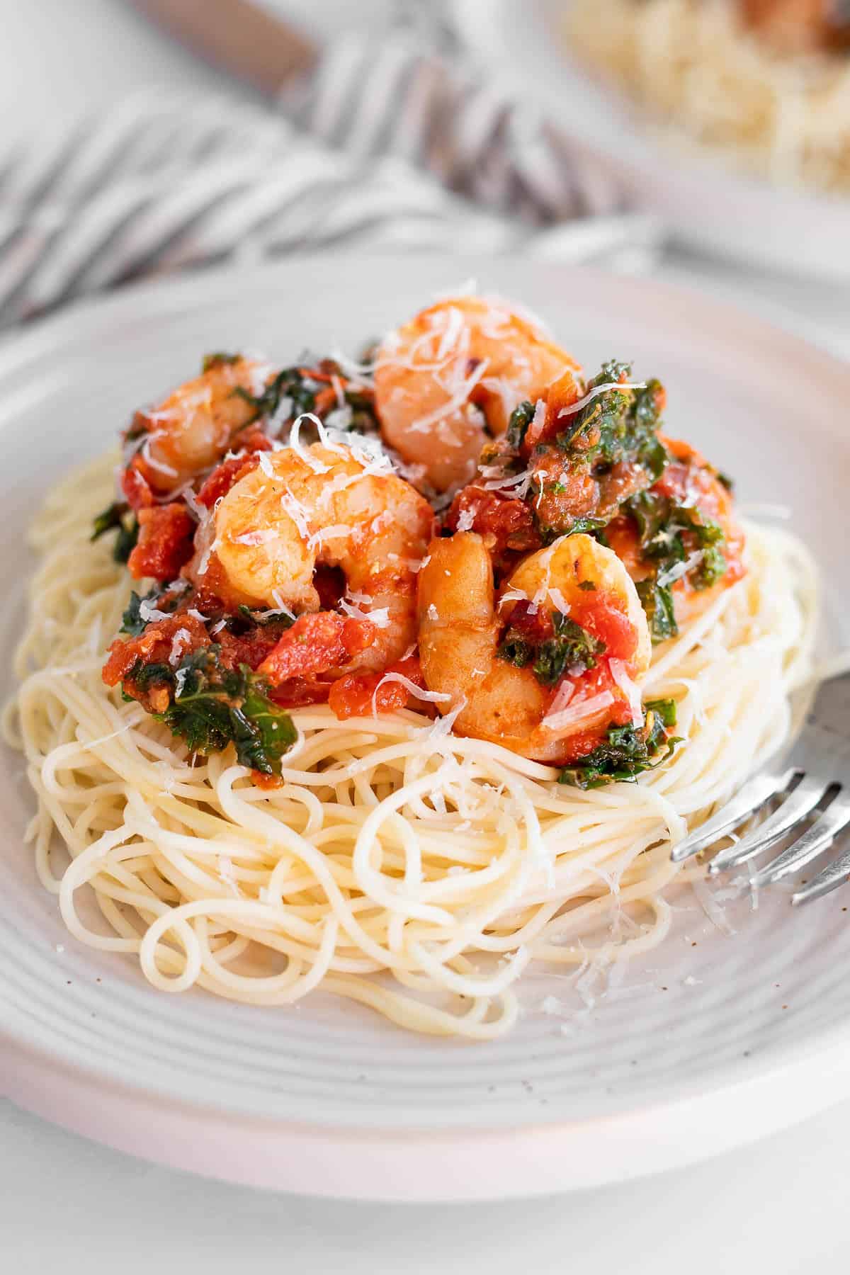Spicy shrimp and kale served over angel hair pasta on a white plate.