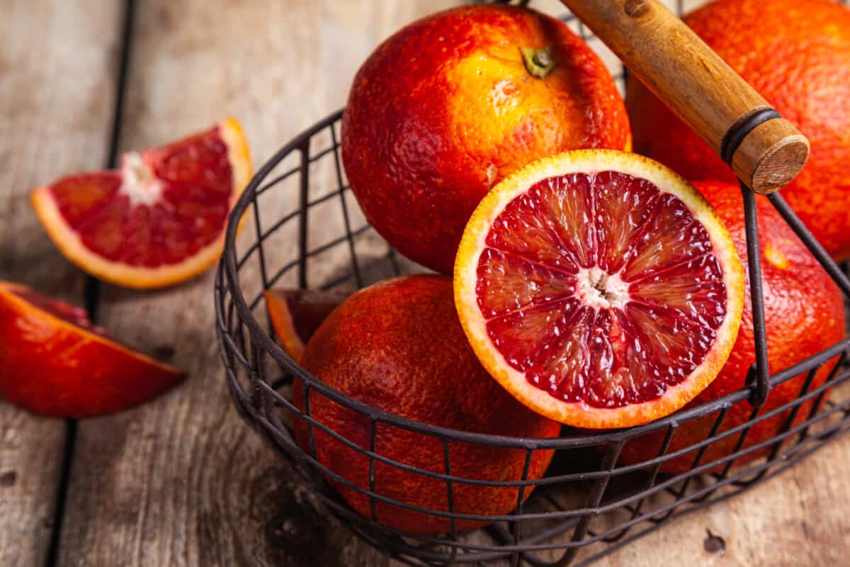 Blood oranges in a metal basket on a wood background.