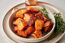 Cinnamon Roasted Sweet Potatoes in a white dish garnished with thyme with honey in the background.