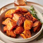 Cinnamon Roasted Sweet Potatoes in a white dish with a sprig of thyme.
