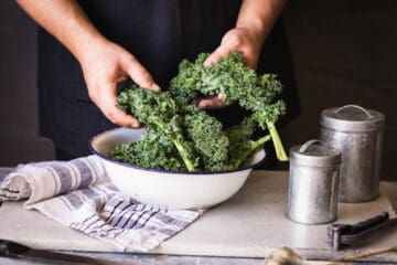 Man holding kale leaves over a bowl on a kitchen counter.